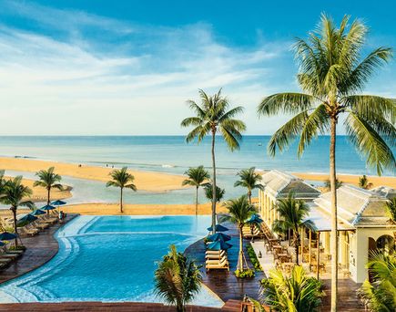 Blick auf den Poolbereich mit Palmen und Liegen des Devasom Khaolak Beach Resort & Villa am Strand unter blauem Himmel