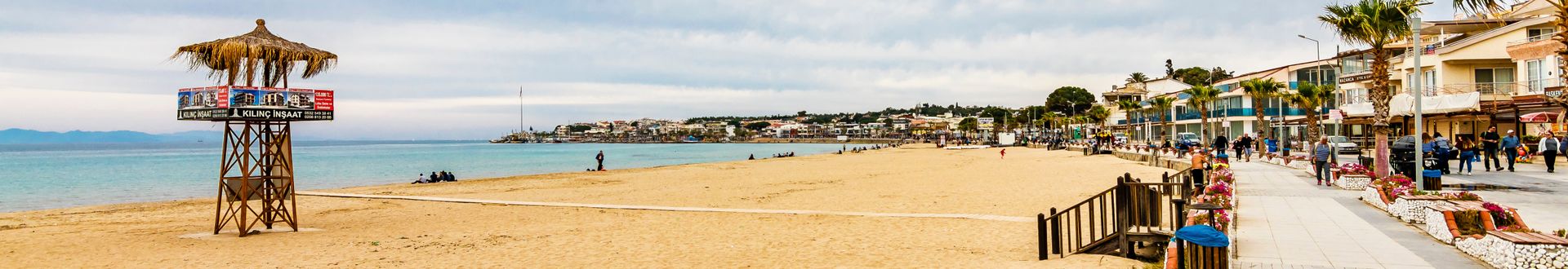 Heller Sandstrand in Didim mit ruhigem Wasser, Promenade, kleinen Geschäften und Spaziergängern entlang der Küste