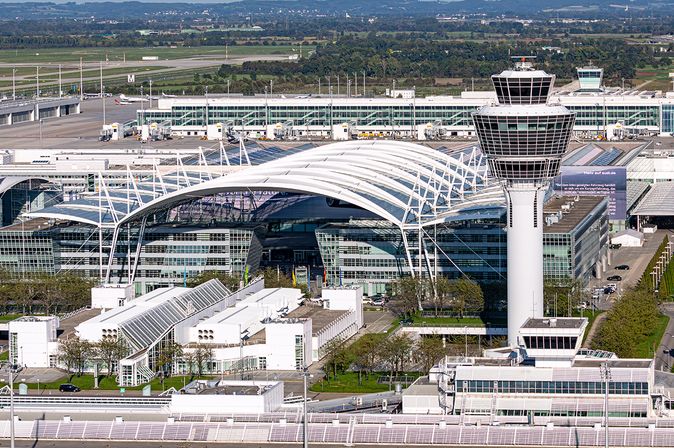 Luftaufnahme des München Airport Centers am Flughafen München mit markanter geschwungener Dachkonstruktion und Kontrollturm, umgeben von Terminalgebäuden, Vorfeld und Start- und Landebahnen