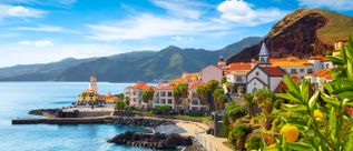 Küstenort Caniçal auf Madeira mit rot gedeckten Häusern, Leuchtturm, Palmen und Blick auf die Atlantikküste vor bergiger Landschaft