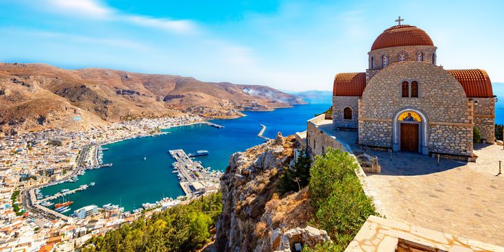 Blick von einem Hügel auf eine Hafenbucht mit einem steinernen Kirchgebäude mit Kuppel im Vordergrund und einer Stadt am Wasser im Hintergrund