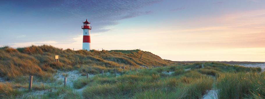 Leuchtturm auf einer Dünenlandschaft mit Gras unter einem bewölkten Himmel bei Sonnenuntergang