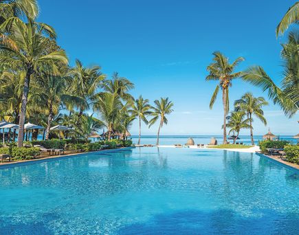 Großer Pool mit klarem Wasser umgeben von Palmen und Liegen mit Sonnenschirmen am Strand des Sugar Beach Mauritius Hotels