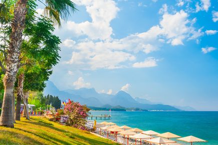 Strandpromenade in Kemer mit Palmen, bunten Blumen und Blick auf das türkisfarbene Meer sowie das Taurusgebirge im Hintergrund