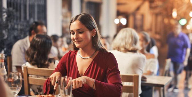 Junge Frau sitzt in einem Restaurant im Freien und genießt ihr Abendessen in gemütlicher Atmosphäre