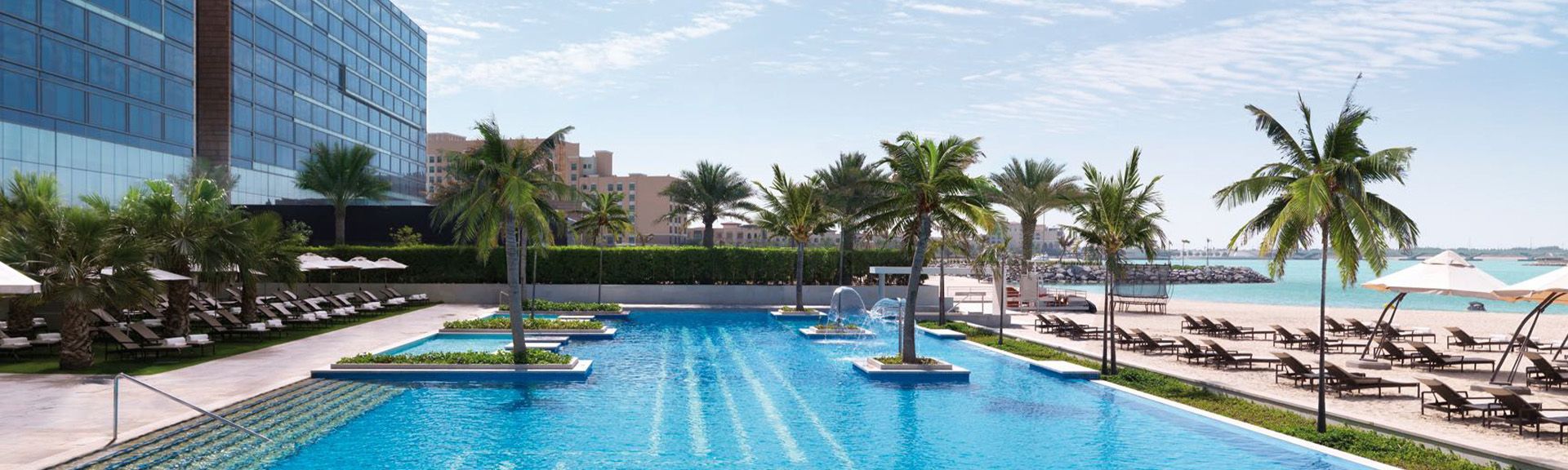 Großer Außenpool mit Inseln und Palmen im Hotel Fairmont Bab Al Bahr in Abu Dhabi, umgeben von Liegestühlen und Sonnenschirmen.