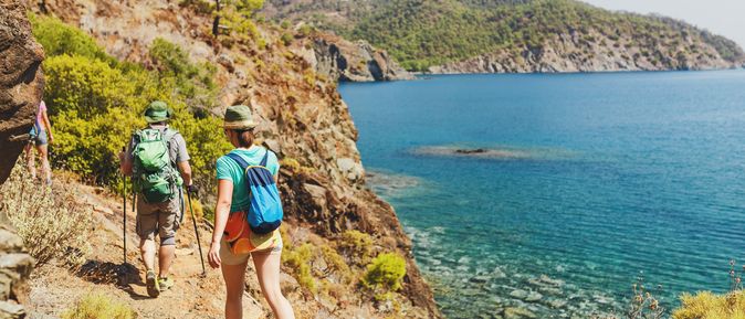 Gruppe von Wandernden auf einem Küstenpfad mit Blick auf das türkisblaue Meer und bewaldete Hügel