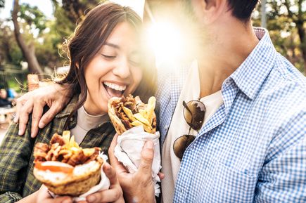 Junges Paar isst Kebab im Fladenbrot im Freien, lacht und hält die gefüllten Wraps in der Hand