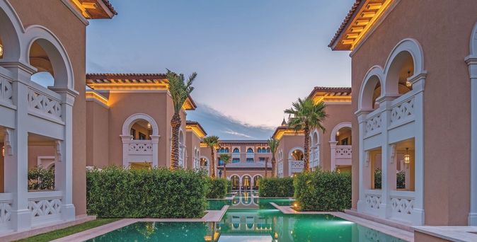 nnenhof des Rixos Premium Saadiyat Island mit symmetrischen, zweistöckigen Gebäuden, Palmen und einem langen Wasserbecken bei Sonnenuntergang