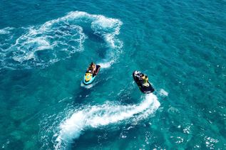 Zwei Jetskis fahren über das türkisfarbene Meer und hinterlassen weiße Wasserwirbel