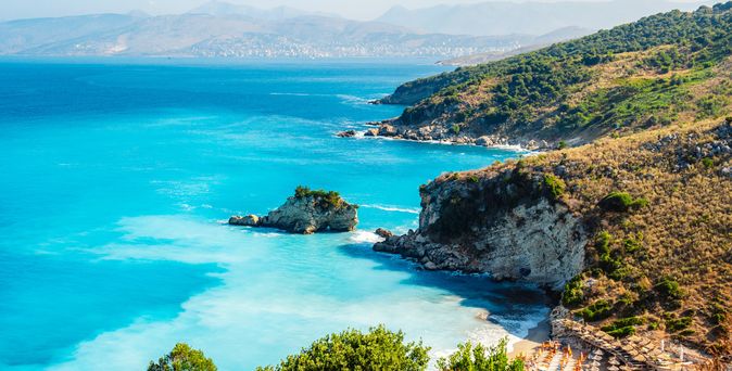 Küste mit felsigen Klippen und türkisfarbenem Meer unter bewölktem Himmel