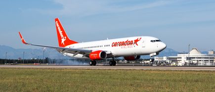 Corendon-Airlines-Boeing-737-800 rollt auf der Startbahn eines Flughafens, rotes Leitwerk und Triebwerke, Terminalgebäude im Hintergrund.