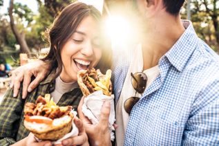 Junges Paar isst Kebab im Fladenbrot im Freien, lacht und hält die gefüllten Wraps in der Hand