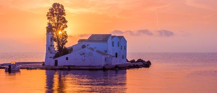 Kirchengebäude auf kleiner Insel bei Sonnenuntergang mit orangefarbenem Himmel und ruhigem Wasser