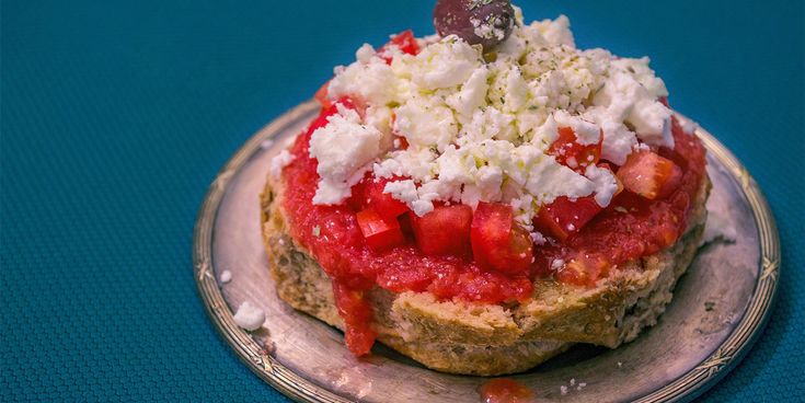 Offenes Vollkornbrot mit Tomatenstücken, Tomatenpüree und zerbröseltem weißen Käse auf einem grauen Teller.