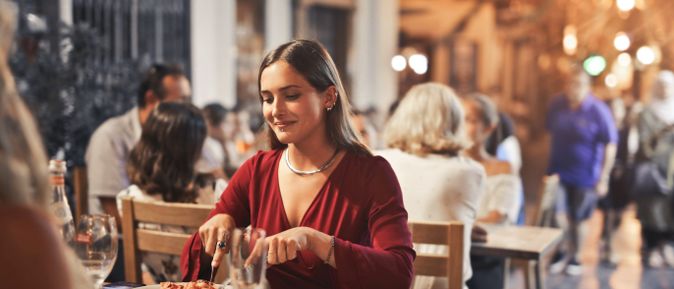Junge Frau sitzt in einem Restaurant im Freien und genießt ihr Abendessen in gemütlicher Atmosphäre