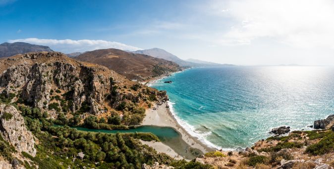 Panoramablick auf den Strand von Preveli auf Kreta, mit klarem Wasser, Sandstrand und umgebenden Bergen.
