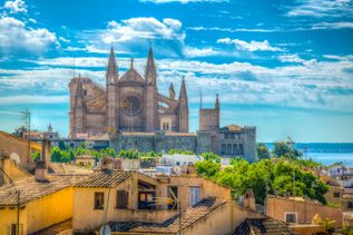 Gotische Kathedrale La Seu in Palma de Mallorca mit spitzen Türmen und Rosettenfenster über den Dächern der Stadt und Blick auf das Meer