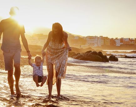 Familie mit zwei Kindern geht bei Sonnenuntergang am Strand im flachen Wasser entlang