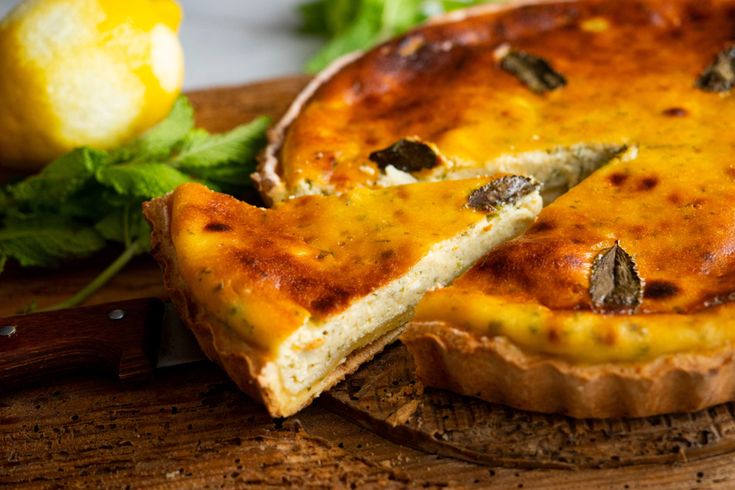Traditioneller Käsekuchen Flaó mit angeschnittenem Stück, garniert mit Minze und Zitrone im Hintergrund