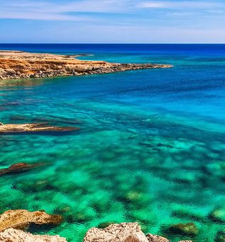 Klares türkisfarbenes Meer an felsiger Küste in Zypern unter blauem Himmel