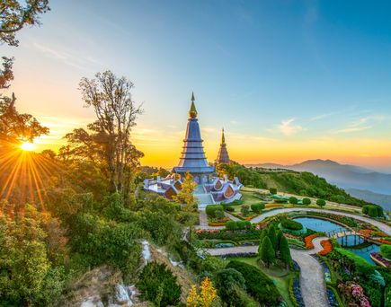 Zwei kunstvolle Stupas (buddhistische Bauwerke) auf einem Berg, umgeben von Gartenanlagen, mit Sonnenaufgang im Hintergrund.