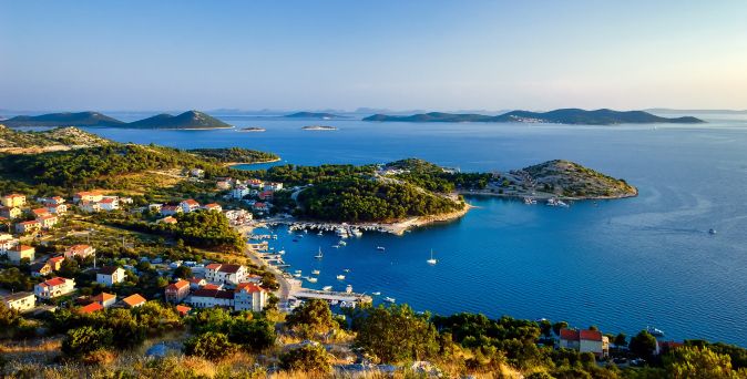 Panoramablick auf die Kornaten in Kroatien mit einer Küstenbucht, kleinen Hafenanlagen, roten Hausdächern und zahlreichen Inseln im tiefblauen Adriatischen Meer