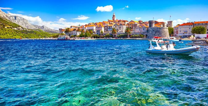 Historische Altstadt von Korčula in Kroatien mit mittelalterlichen Steinmauern, Kirchturm, Hafenbereich und klarem Adriatischen Meer im Vordergrund