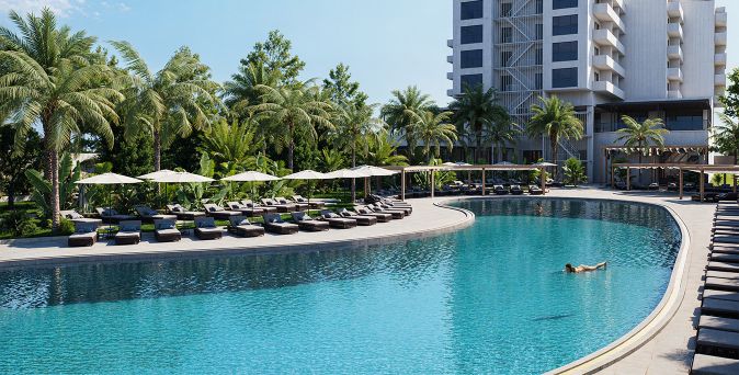 Großer, geschwungener Hotelpool mit Liegen und Sonnenschirmen am Rand, umgeben von Palmen und einem mehrstöckigen Hotelgebäude im Hintergrund.
