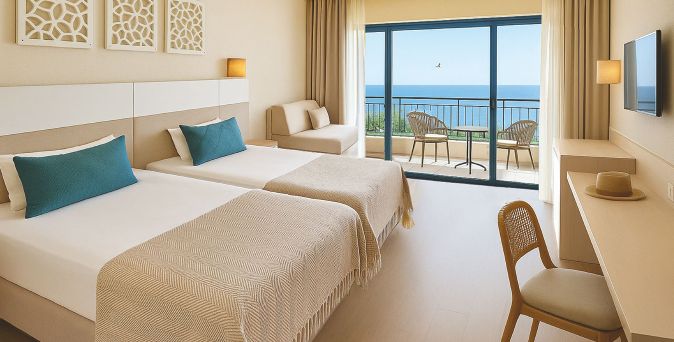 Helles und modernes Hotelzimmer mit beigen und türkisfarbenen Akzenten mit zwei Einzelbetten, Sitzbereich, Schreibtisch und Balkon mit Meerblick.