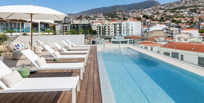 Dachterrasse mit Pool und Liegestühlen vor Stadt- und Bergkulisse.