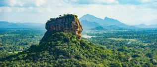 Pidurangala Rock in Sri Lanka erhebt sich über eine bewaldete Landschaft mit Bergen und Ebenen im Hintergrund