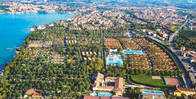 Luftaufnahme des Campingplatzes Bella Italia am Gardasee mit Zelten, Wohnmobilen, Schwimmbädern und Tennisplätzen in einer weitläufigen, grünen Anlage.