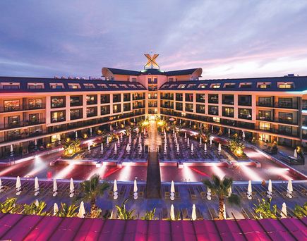 Das Hotel The X Belek mit beleuchtetem Poolbereich und mehreren Etagen mit Balkonen bei Dämmerung