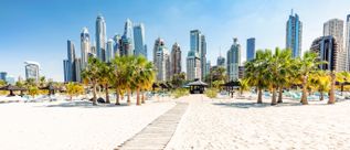 Sandstrand der Jumeirah Beach Residence in Dubai mit Palmen, Strandliegen und moderner Skyline im Hintergrund