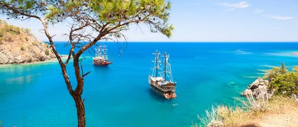 Türkise Bucht bei Kemer an der Türkischen Riviera mit zwei traditionellen Segelschiffen und bewaldeten Felsklippen