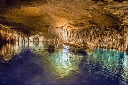 Boot fährt auf einem unterirdischen See in den Tropfsteinhöhlen Cuevas del Drach, beleuchtet von warmem Licht