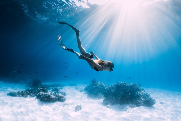 Frau mit Schwimmflossen beim Tauchen und Sonnenstrahlen unter Wasser
