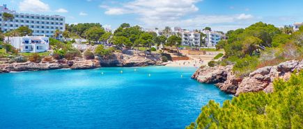 Türkisfarbene Bucht Cala Esmeralda in Cala d’Or auf Mallorca, umgeben von Felsen, Pinien und weißen Häusern