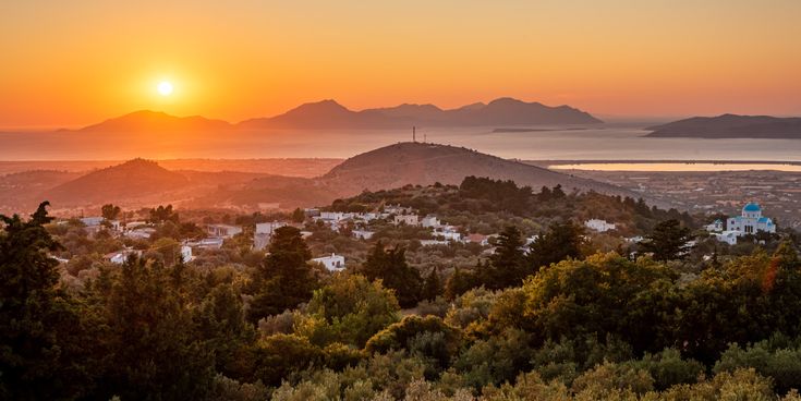 Sonnenuntergang über hügeliger Landschaft mit weiß getünchten Häusern und einer Kirche mit blauem Kuppeldach