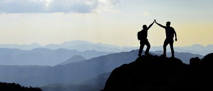 Zwei Bergsteiger geben sich High Five auf Berggipfel bei Sonnenuntergang