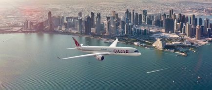 Qatar Airways Airbus A350‑1000 über der Küste von Doha mit moderner Skyline im Hintergrund