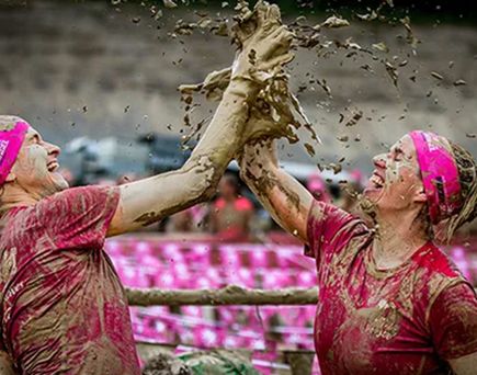 Zwei Teilnehmende beim Muddy Angel Run geben sich mit schlammigen Händen ein High Five