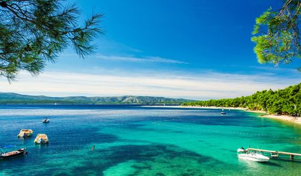 Golden Cape Beach in Istrien in Kroatien mit türkisblauem Meer, kleinen Booten im Wasser, einem abgegrenzten Badebereich und einer grünen Küstenlandschaft unter klarem Himmel
