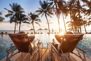 Zwei Personen liegen auf Liegestühlen an einem Pool mit Blick auf Palmen und Sonnenuntergang am Raa-Atoll auf den Malediven