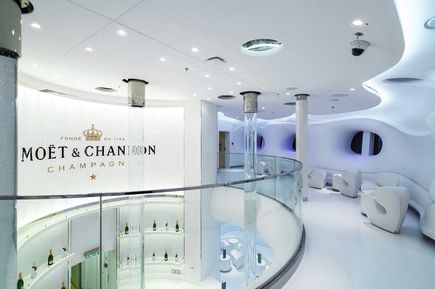 Die exklusive Moët & Chandon Spray-Bar der AIDAprima mit elegantem, weißem Interieur, geschwungenem Design, gläsernem Geländer und stilvoll beleuchteter Champagner-Präsentation