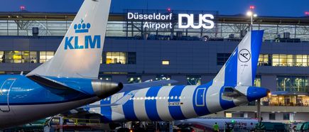 KLM‑ und Lufthansa‑Flugzeuge stehen nachts auf dem Vorfeld am Flughafen Düsseldorf, vor dem beleuchteten Terminalgebäude mit der Aufschrift „Düsseldorf Airport DUS“