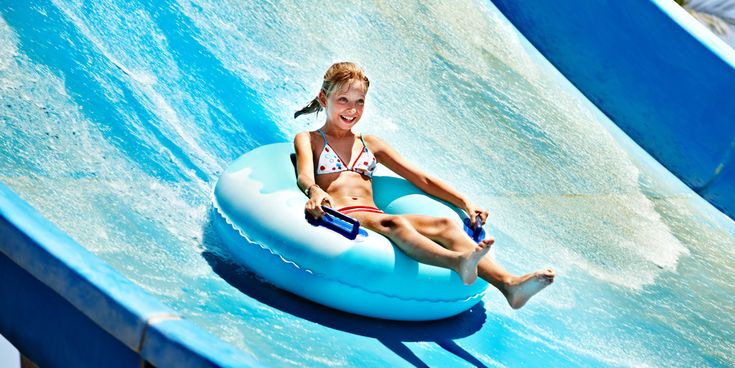 Mädchen rutscht auf einer breiten Wasserrutsche im Schwimmreifen hinunter und lächelt dabei