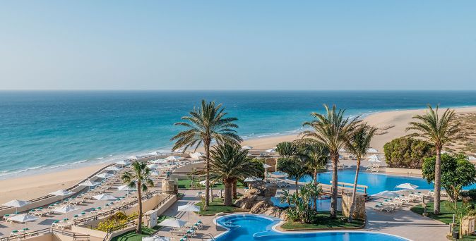 Blick auf den Poolbereich mit mehreren Palmen und Liegen am Strand des Iberostar Waves Playa Gaviotas auf Fuerteventura.