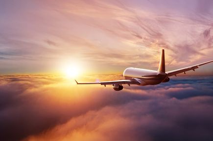 Passagierflugzeug fliegt in Richtung Sonnenuntergang über einer geschlossenen Wolkendecke; stimmungsvolle Himmelsszene im warmen Licht